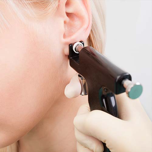 Farmaceutica haciendo una perforación en la oreja a un paciente.
